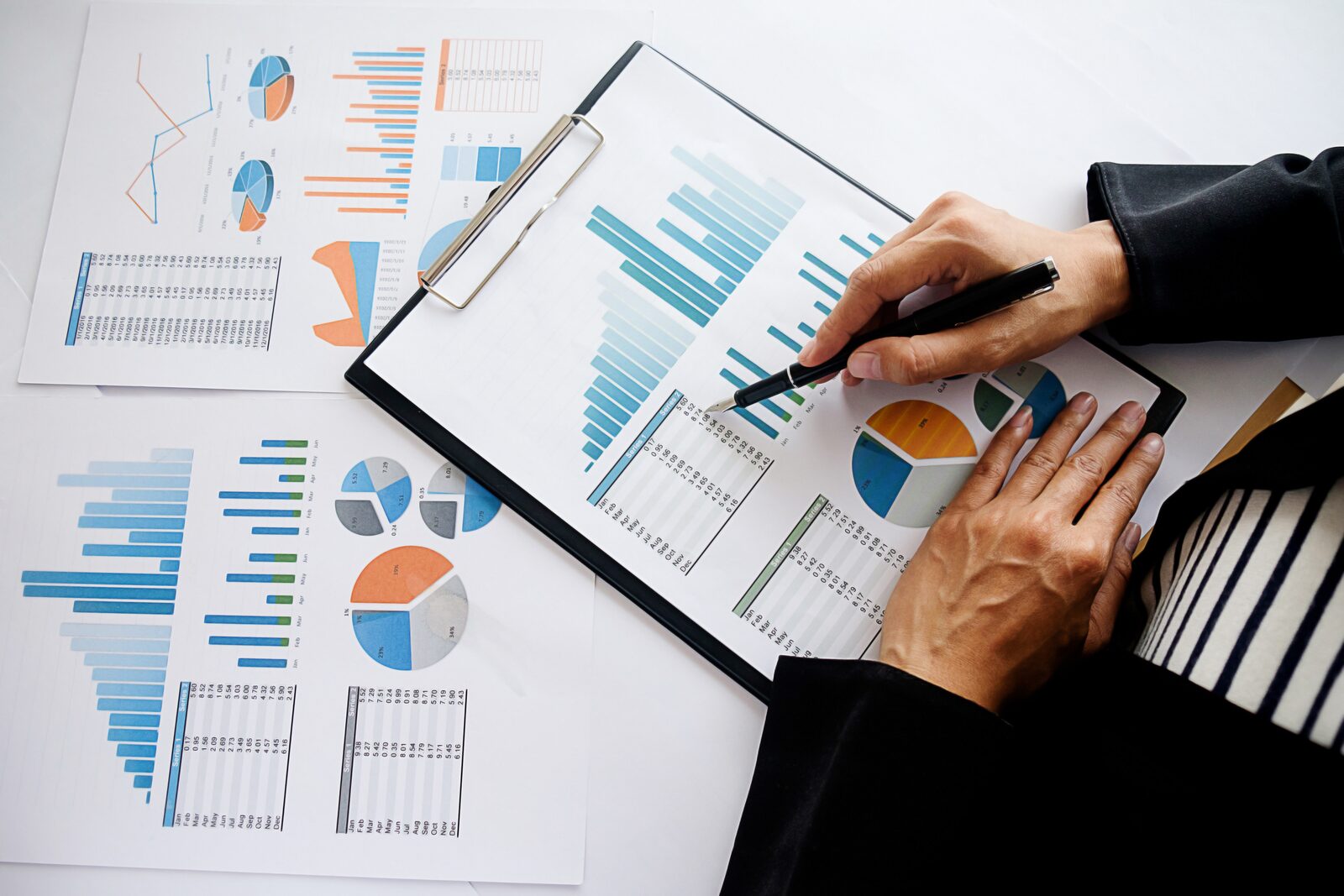 Two hands reviewing printed bar charts, tables and pie charts with a pen
