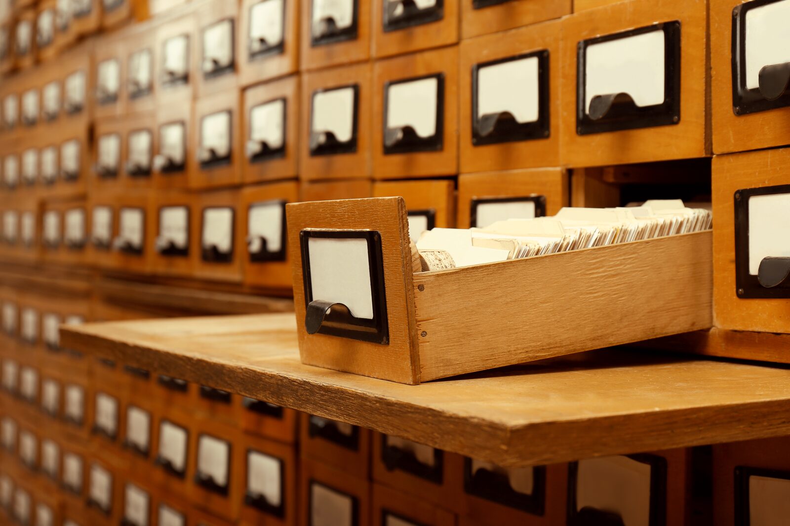 An open wooden library card-catalog drawer surrounded by rows of labeled drawers